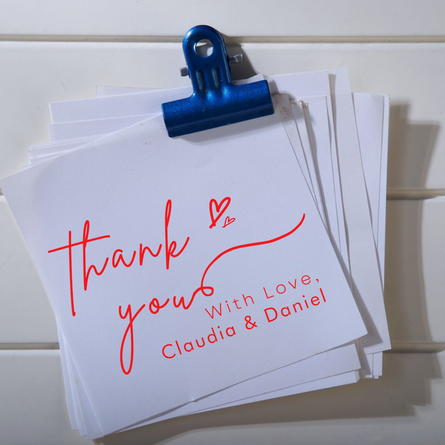 Blue binder clip holding white cards with red thank-you stamp and seal, signed Claudia & Daniel.