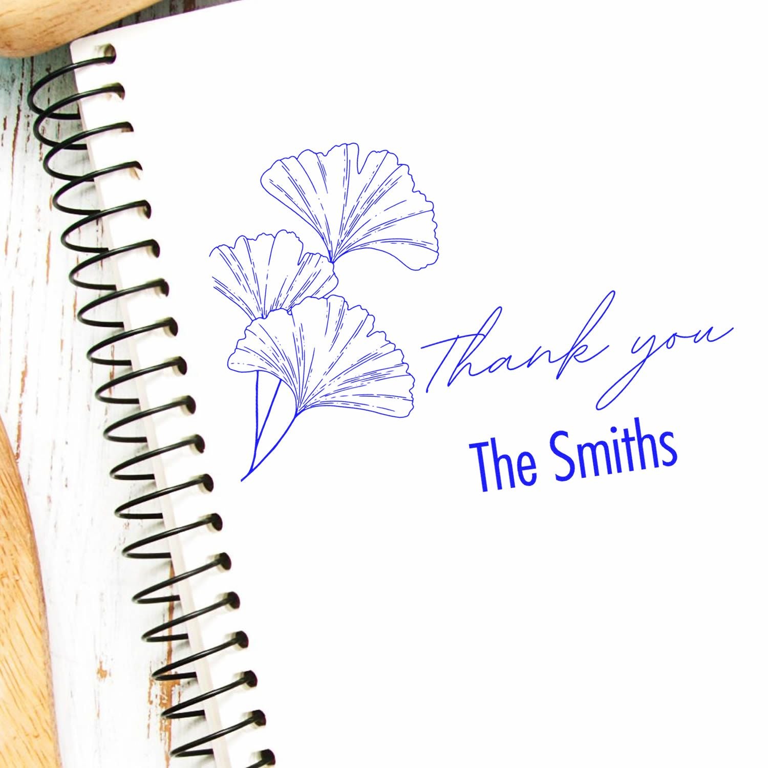 Blue custom stamp and seal featuring ginkgo leaves, Thank you, and The Smiths on a white spiral notebook.