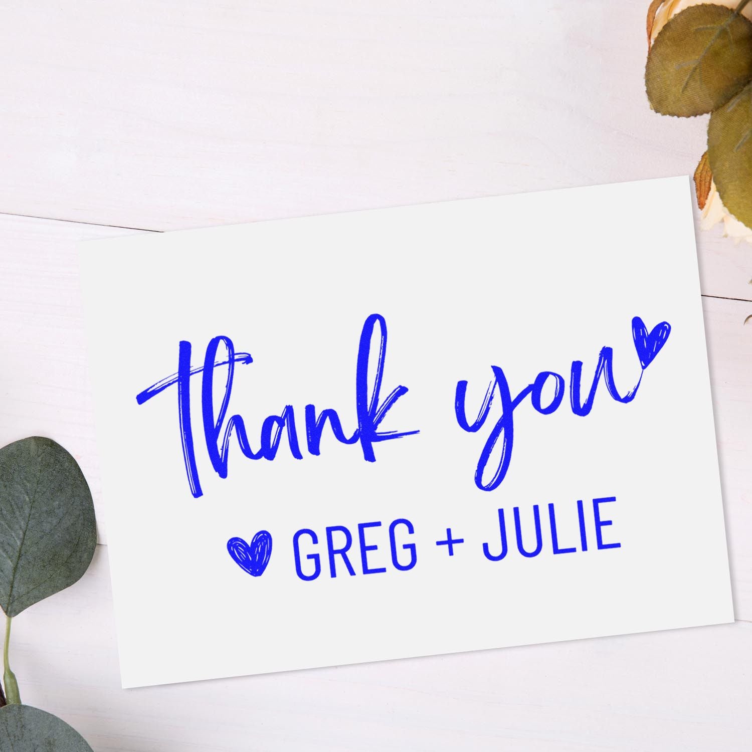 Blue thank you stamp and seal card with heart and Greg + Julie, on white background with eucalyptus leaves.