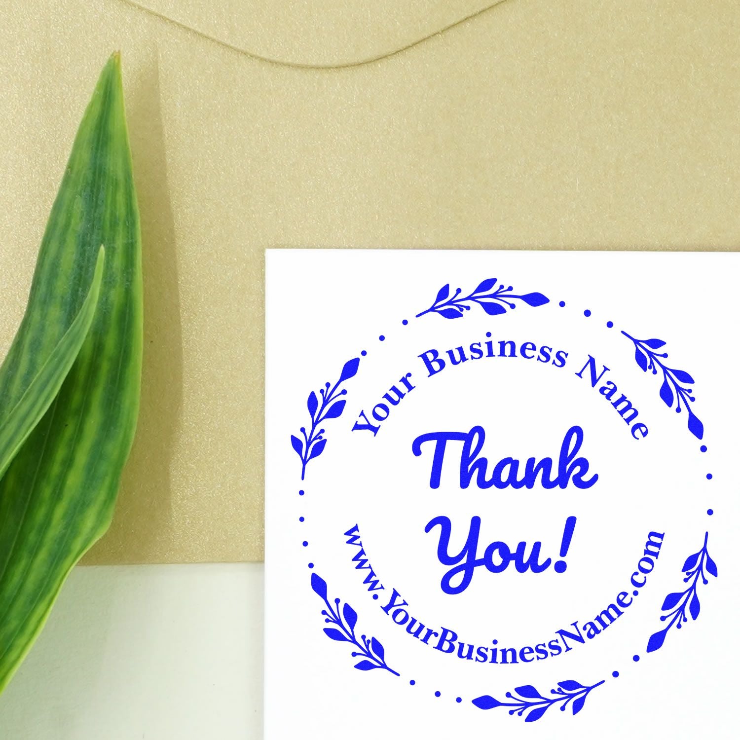 Blue circular thank-you business stamp seal with leafy border on white card, beside a green leaf on beige background.