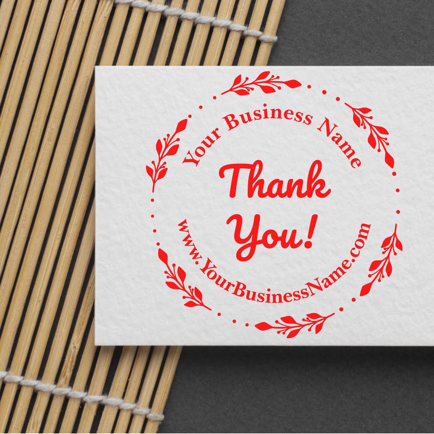 Red custom thank-you stamp seal with floral border and Your Business Name on white paper, on bamboo mat background.
