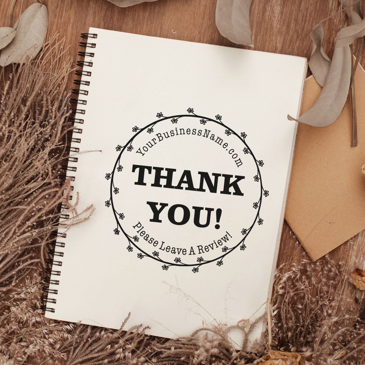White spiral notebook featuring a black custom thank-you review stamp, styled on a rustic brown background with dried foliage.