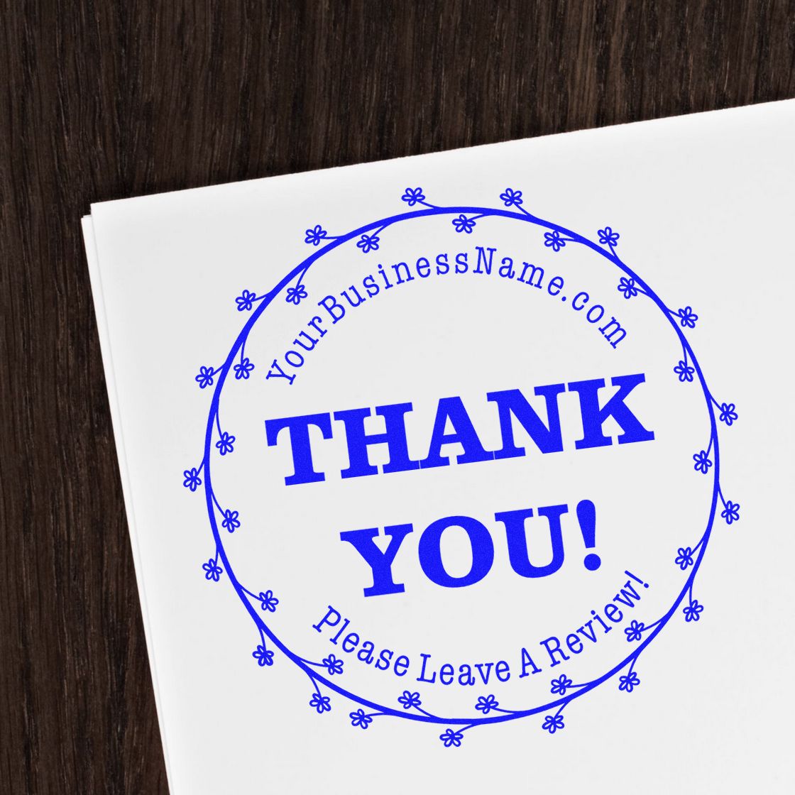 Blue circular thank-you stamp seal with floral border, YourBusinessName.com, on white paper over dark wood.