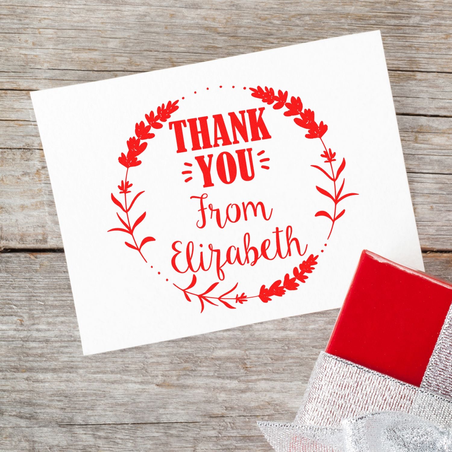 Red thank-you stamp and seal on white card with floral wreath and Elizabeth name, beside a red stamp block on wood.