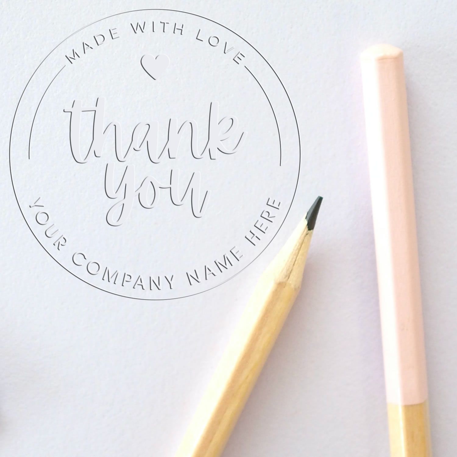 Embossed circular thank you stamp seal on white paper, with pastel pink and gold pencils.