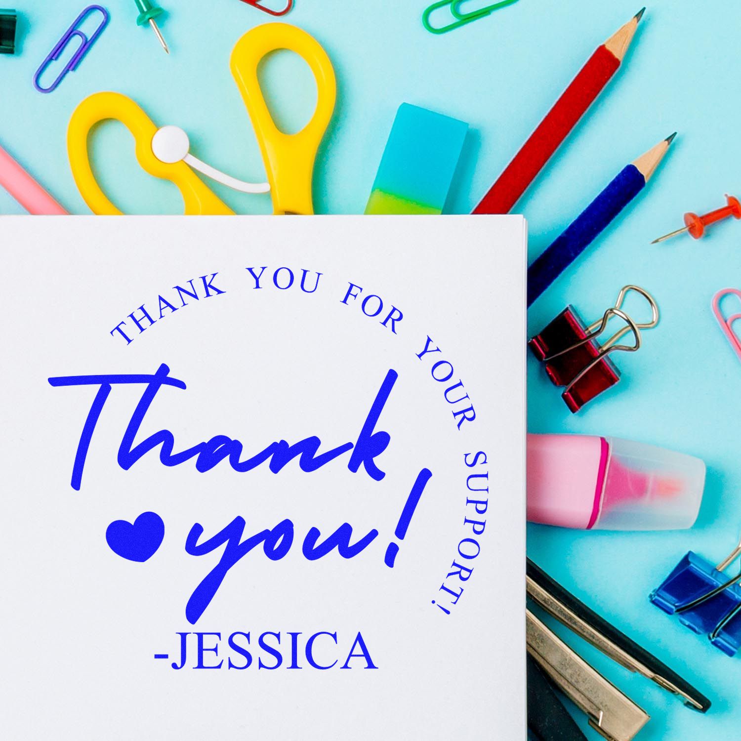 Blue custom thank-you stamp on white card with colorful stationery, stamps and seals on aqua background.