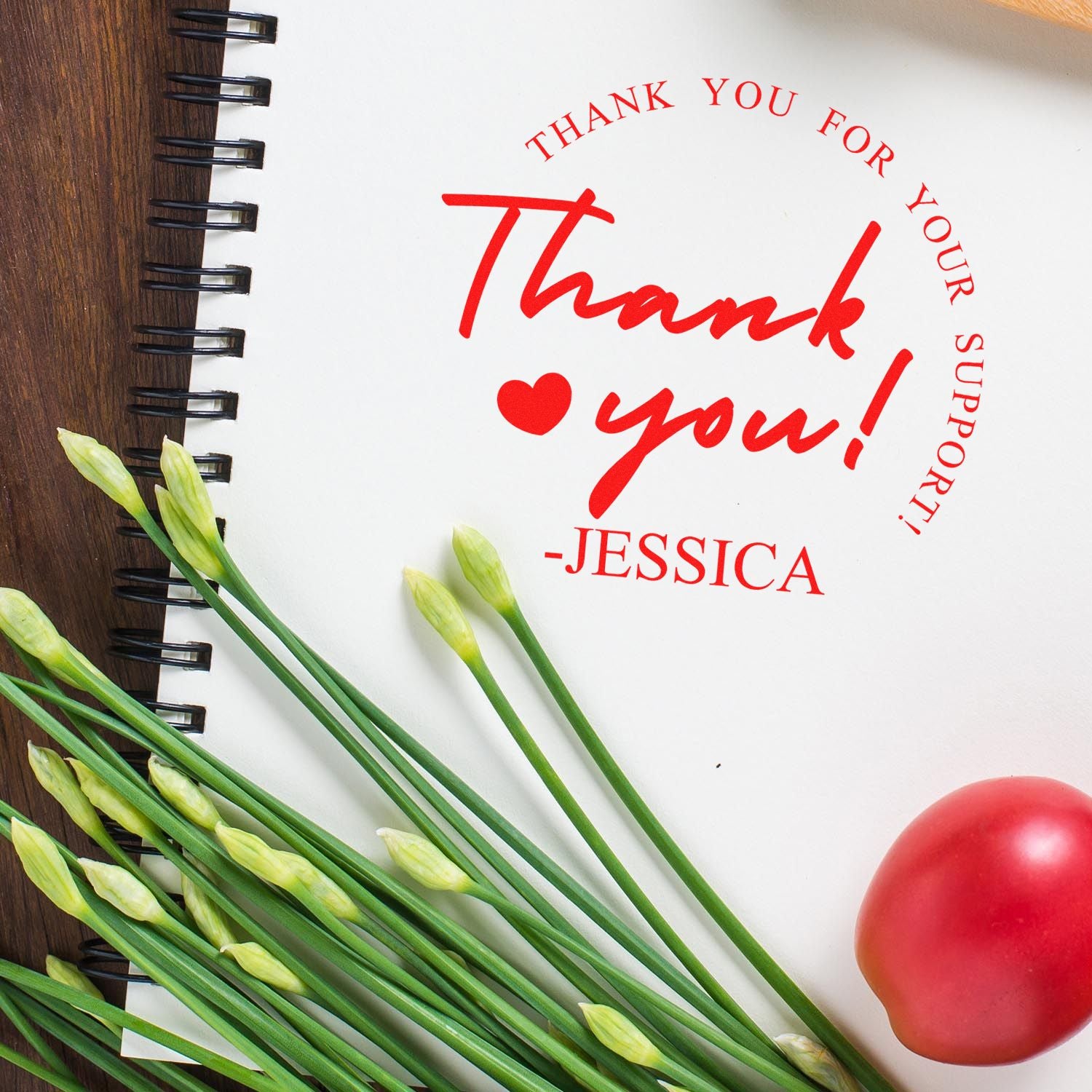 Red thank-you stamp and seal on white spiral notebook, with Jessica signature, heart, and green flower stems.