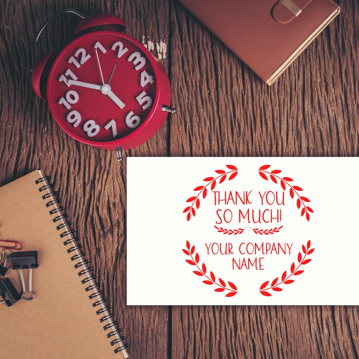 Red custom stamp and seal featuring Thank You So Much in white and red on a wood desk with notebook and brown planner.