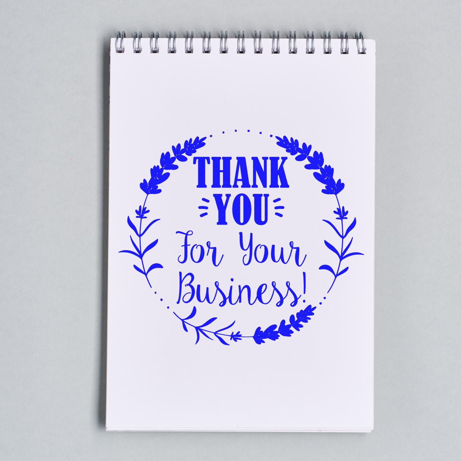 Blue thank-you for your business stamp and seal with floral wreath on a white spiral notepad