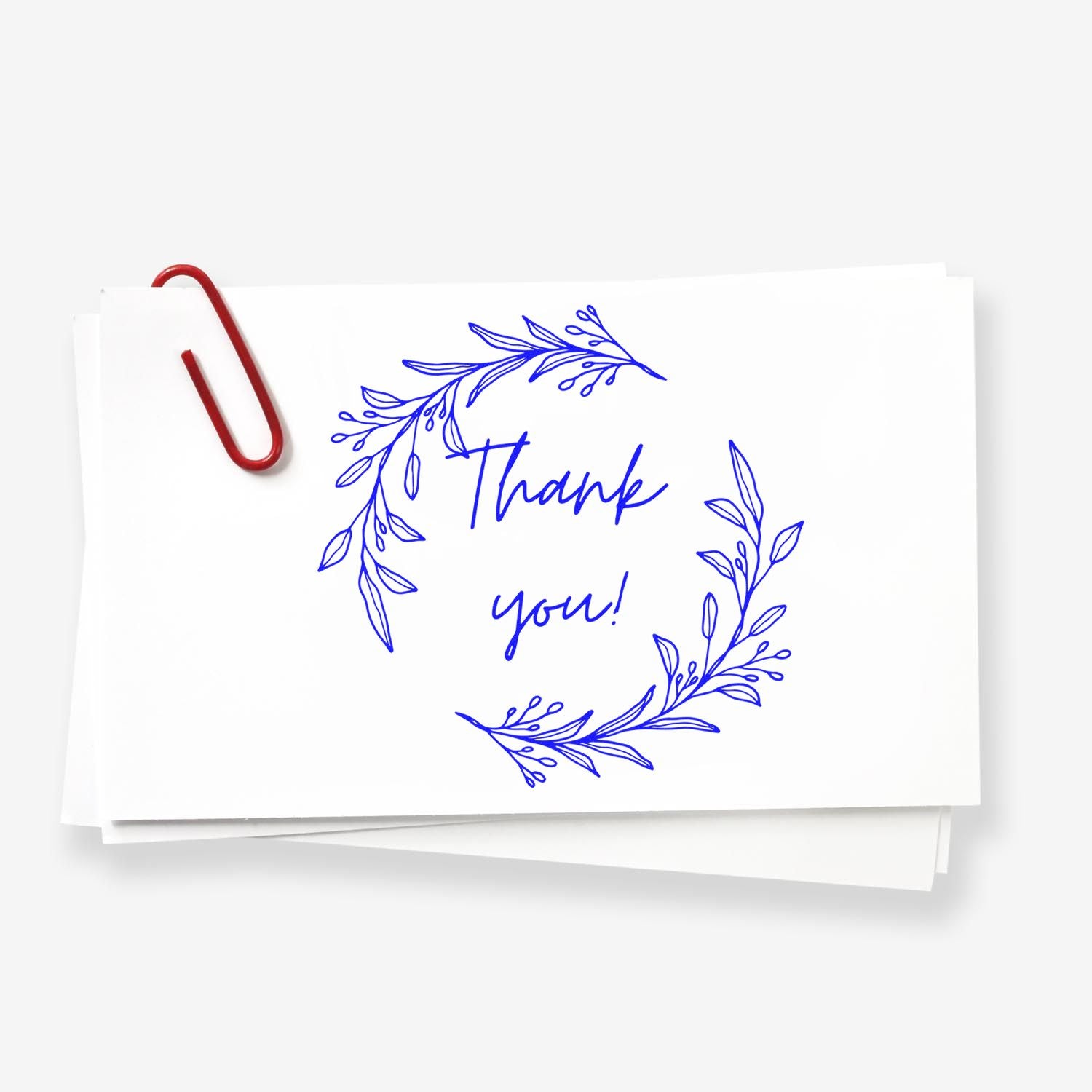 Blue thank-you rubber stamp and seal design with leafy wreath on stacked white cards and a red paperclip.