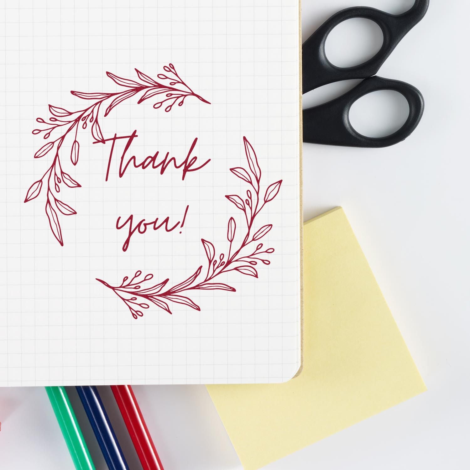 Red floral thank-you stamp and seal design on grid paper, with black scissors, yellow note, and colored pens.