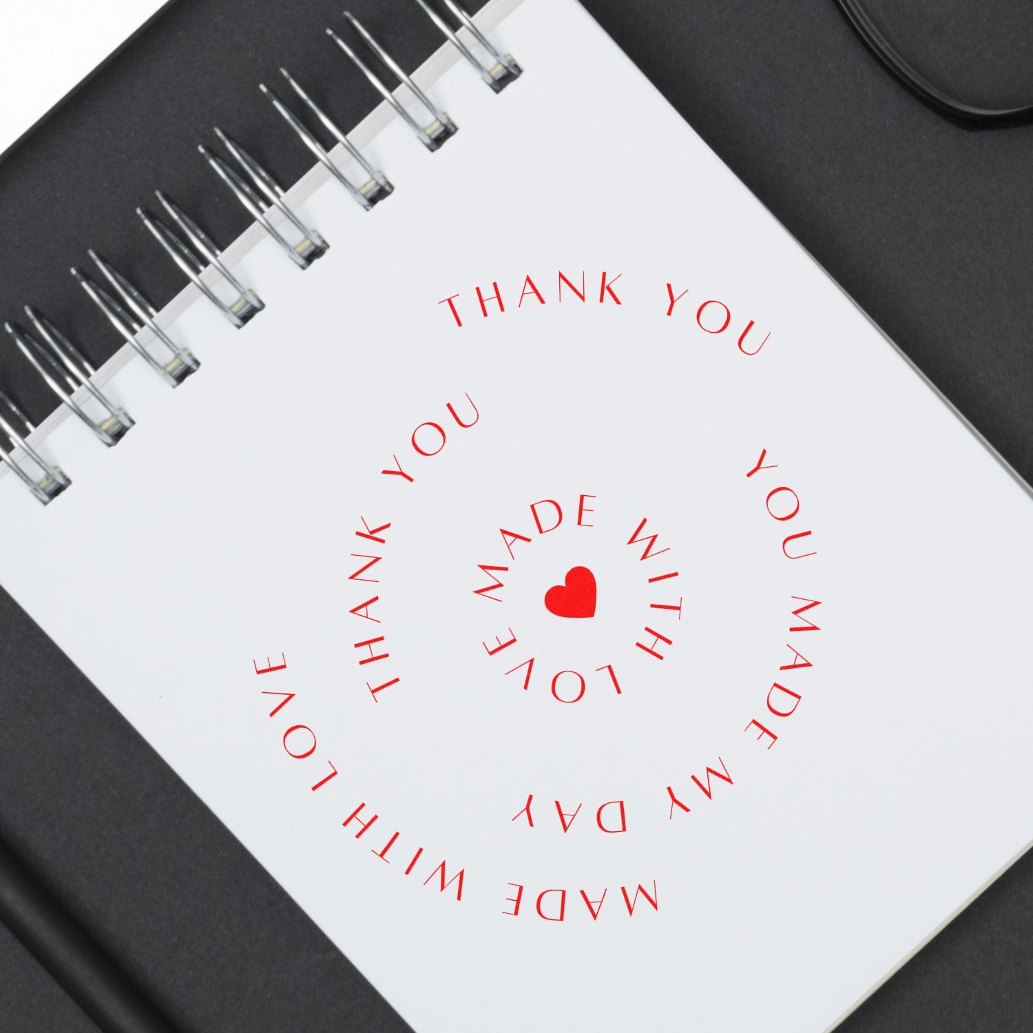 Red thank-you stamp seal with heart on white spiral notebook against black background