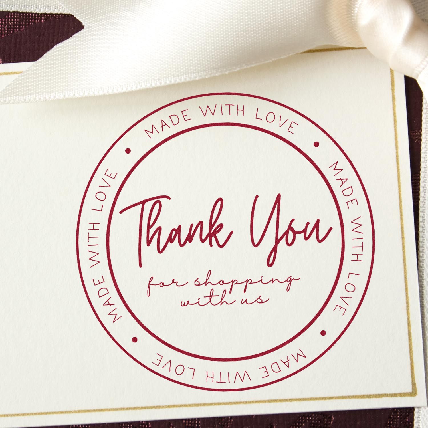 Burgundy circular thank-you stamp seal on white card, with cream ribbon and gold foil border.