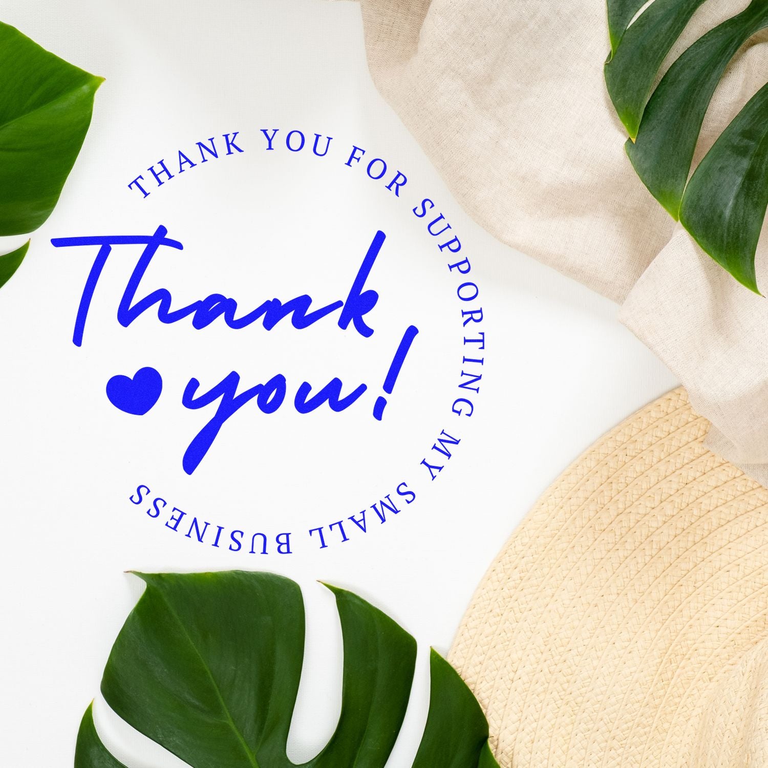 Blue thank you stamp seal with heart and circular text on white, framed by green leaves, beige fabric, and straw hat.