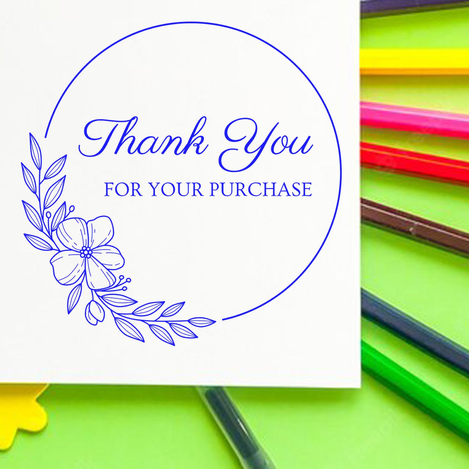 Blue floral thank you for your purchase stamp seal on white square card, set against a bright green background with colorful pencils.