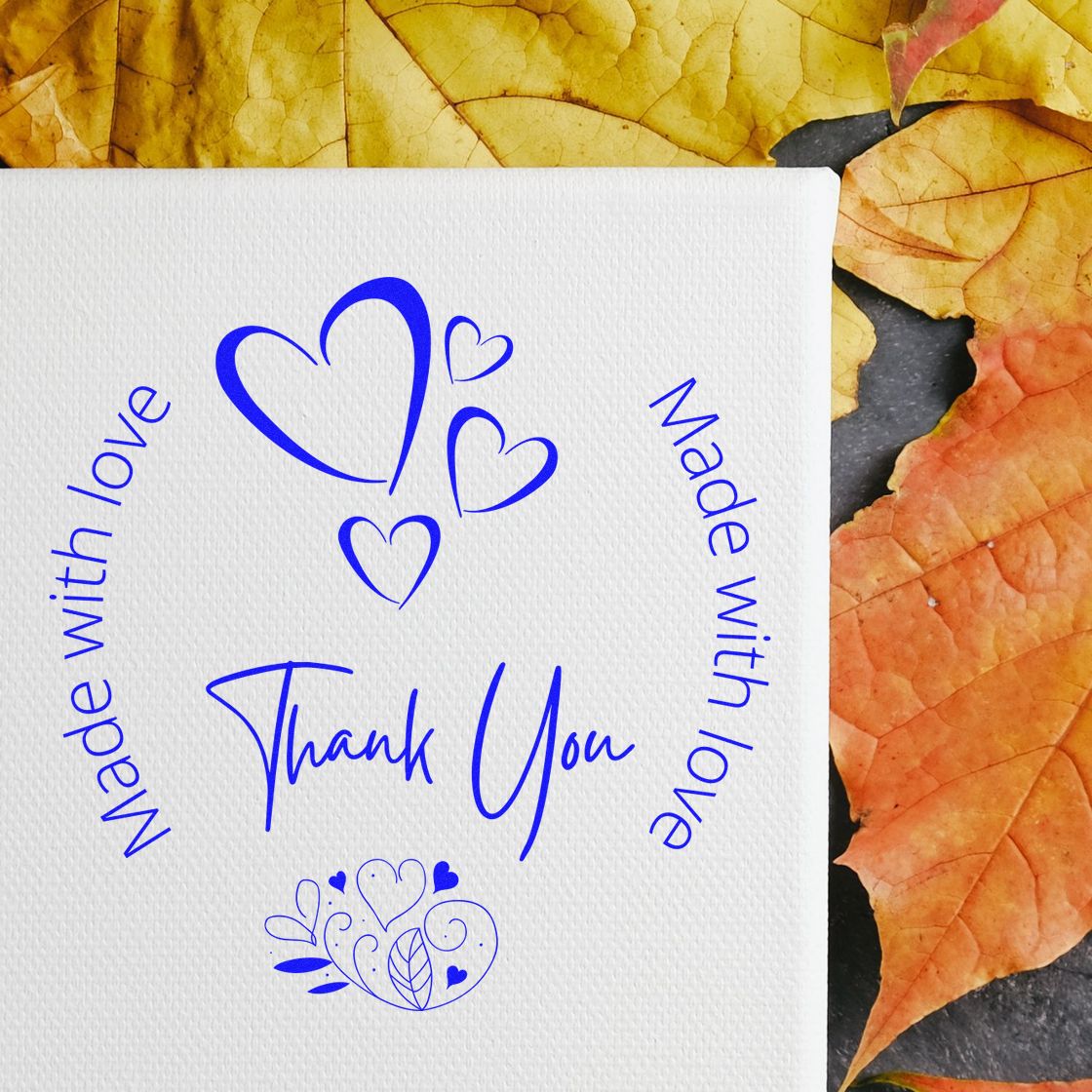 Blue thank-you stamp and seal with heart motifs and Made with love on white paper, bordered by autumn leaves.