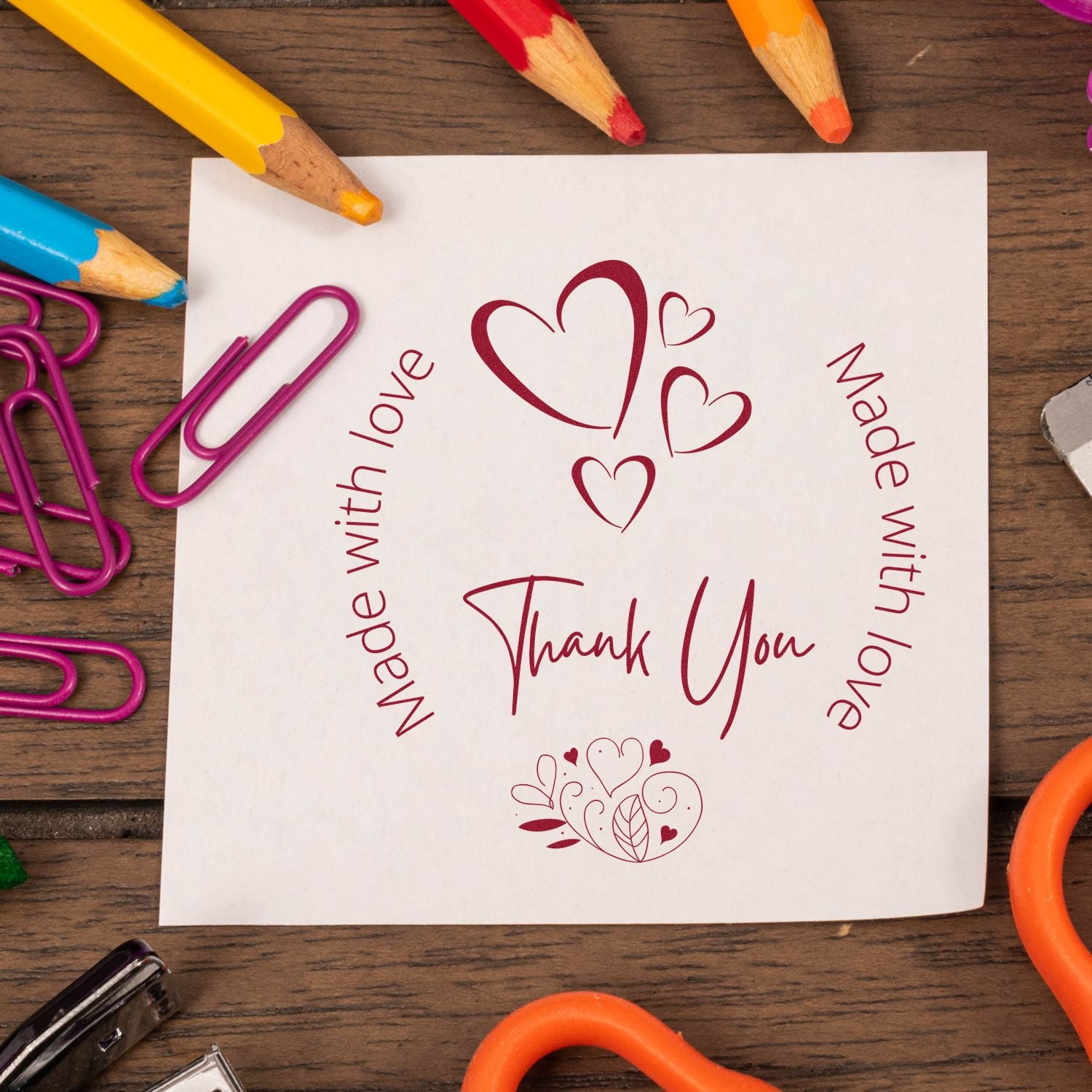 Heart-themed thank you stamp and seal on white paper, surrounded by colorful pencils and magenta paperclips