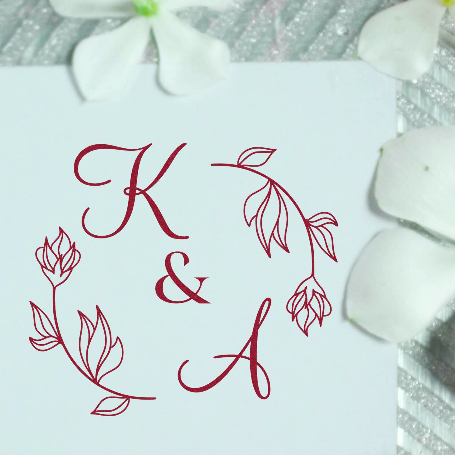Burgundy K and A floral monogram stamp and seal design on a white card, with white petals on a silver textured background.