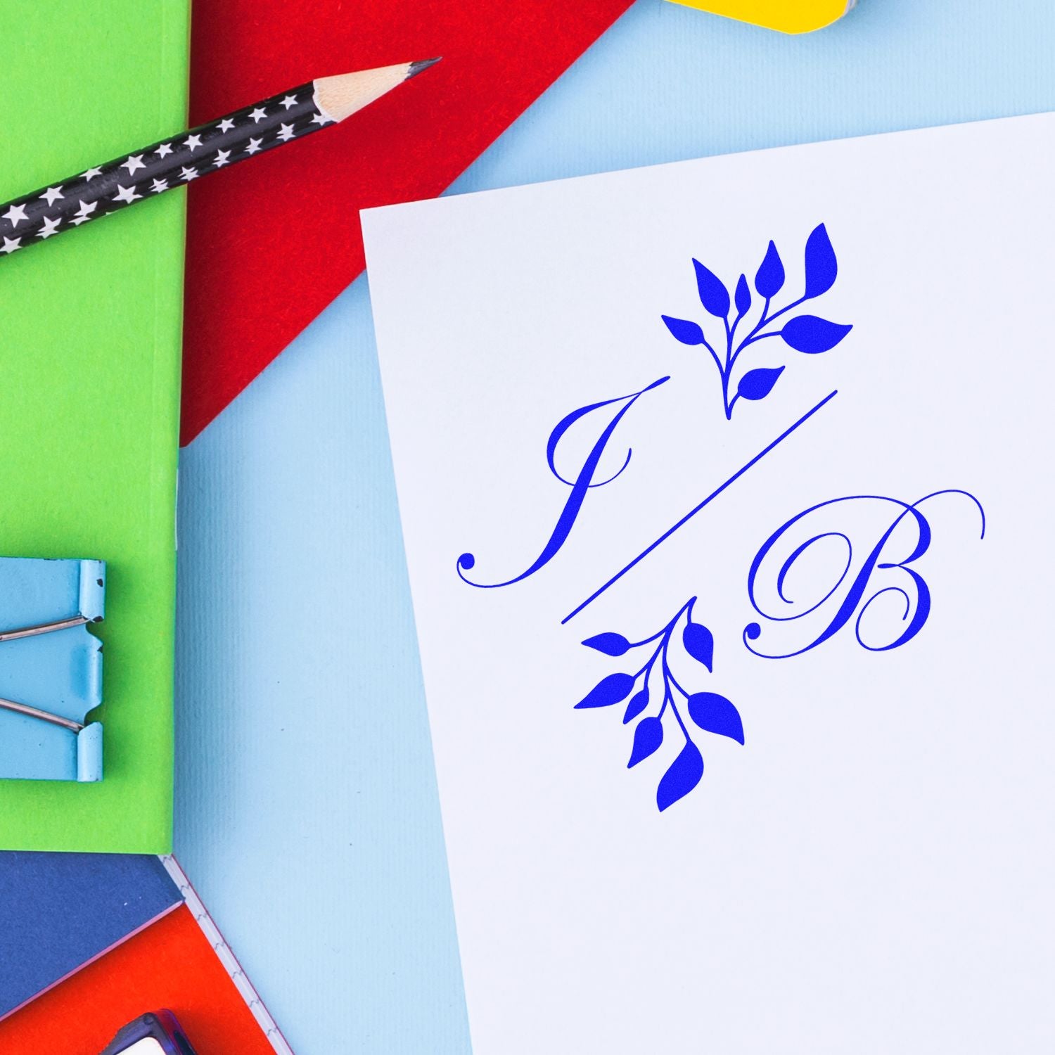 Blue JB monogram stamp and seal on white card with leafy design, colorful stationery, and a star-pattern pencil.