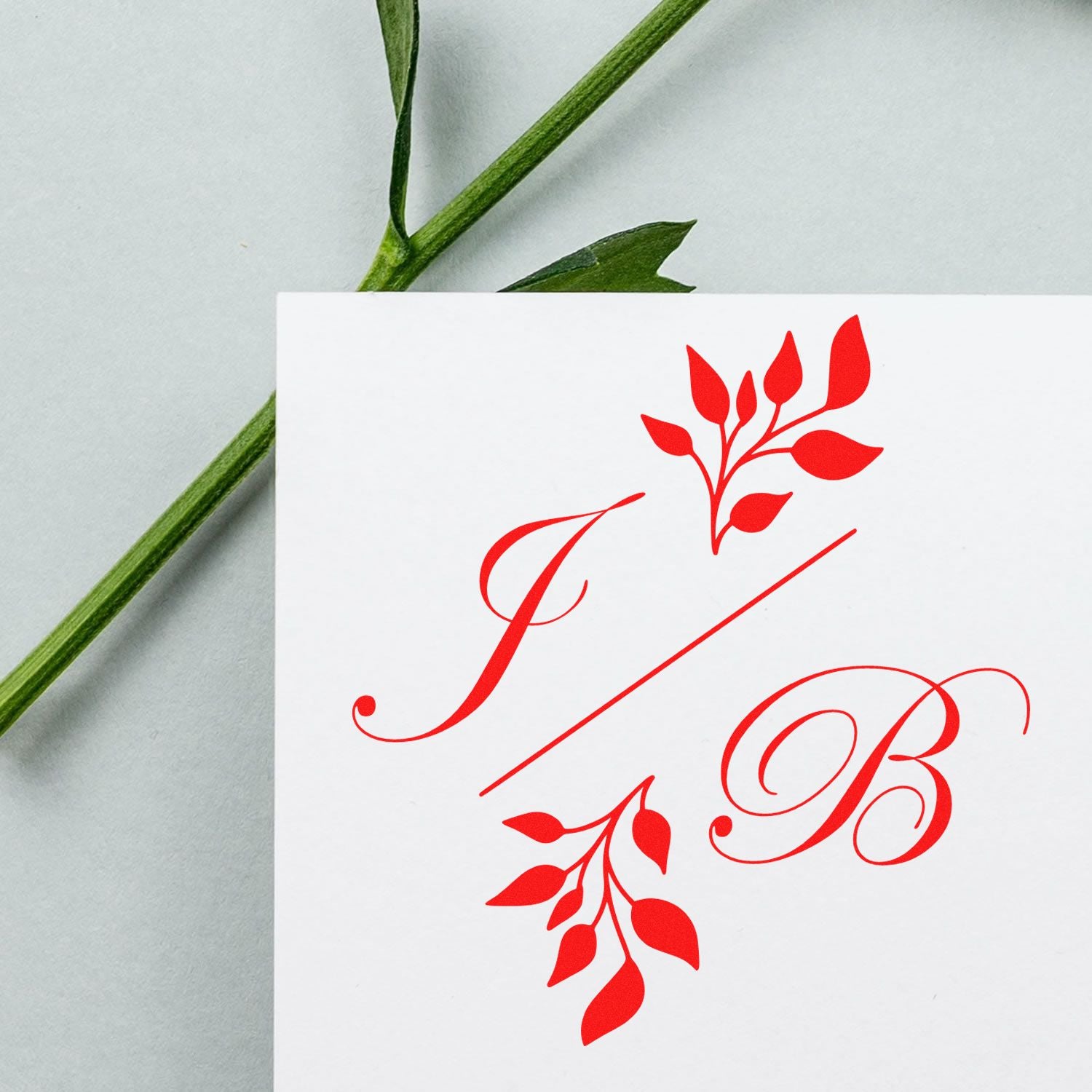 Red custom stamp and seal with floral monogram F/B on white card, beside a green stem