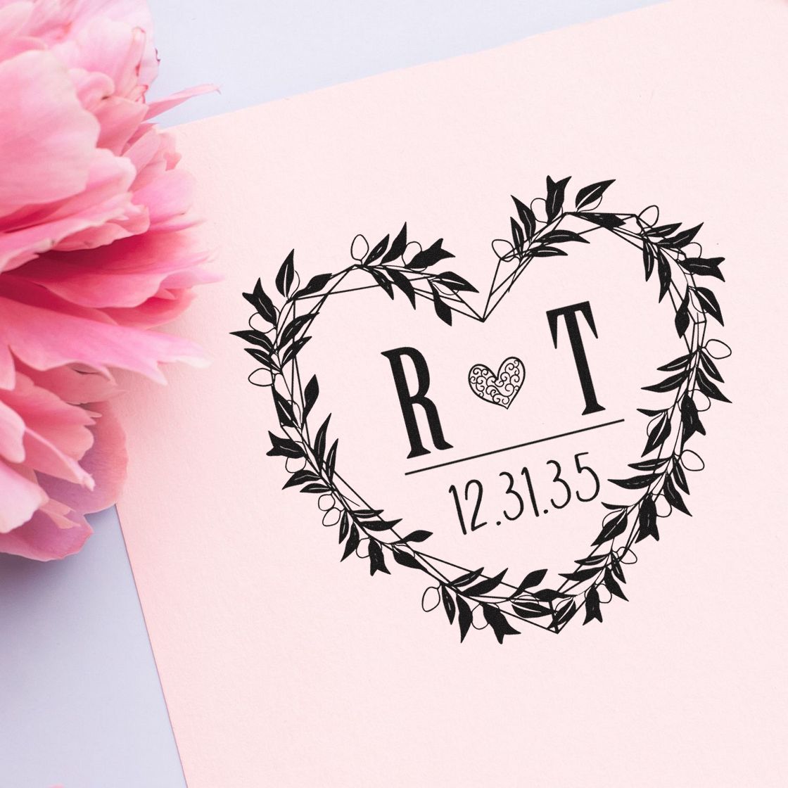 Black floral heart wedding stamp seal on pale pink paper with initials R ? T and date 12.31.35, beside pink peony.