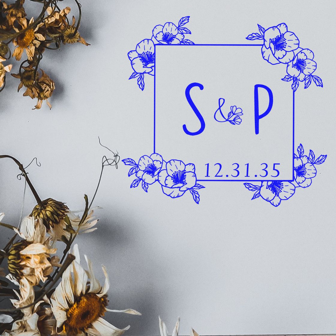 Blue floral monogram stamp and seal with S&P, date 12.31.35, on light gray background with dried flowers.