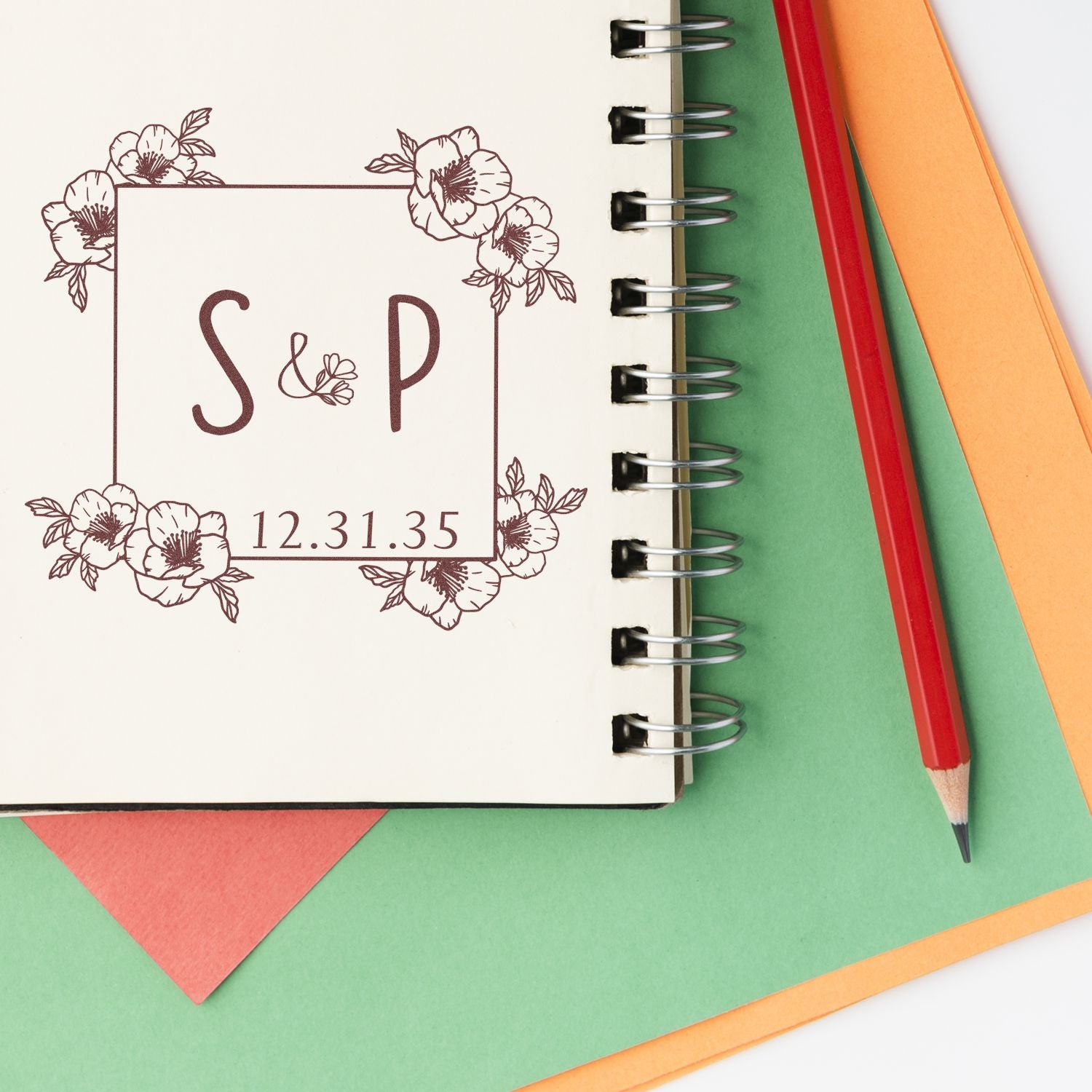 Floral S&P monogram stamp seal with 12.31.35 date on cream notebook, beside red pencil and green, orange, and pink paper