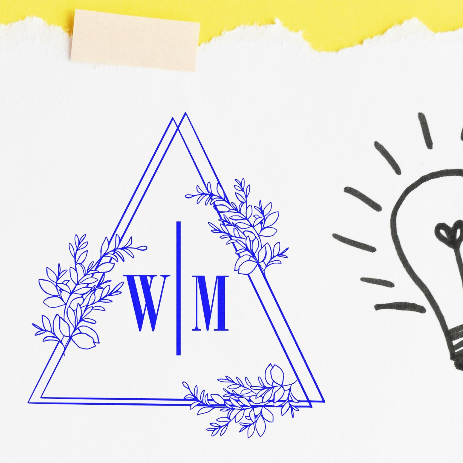 Blue custom monogram stamp seal with W|M inside a triangular floral wreath on white paper with a yellow torn edge.