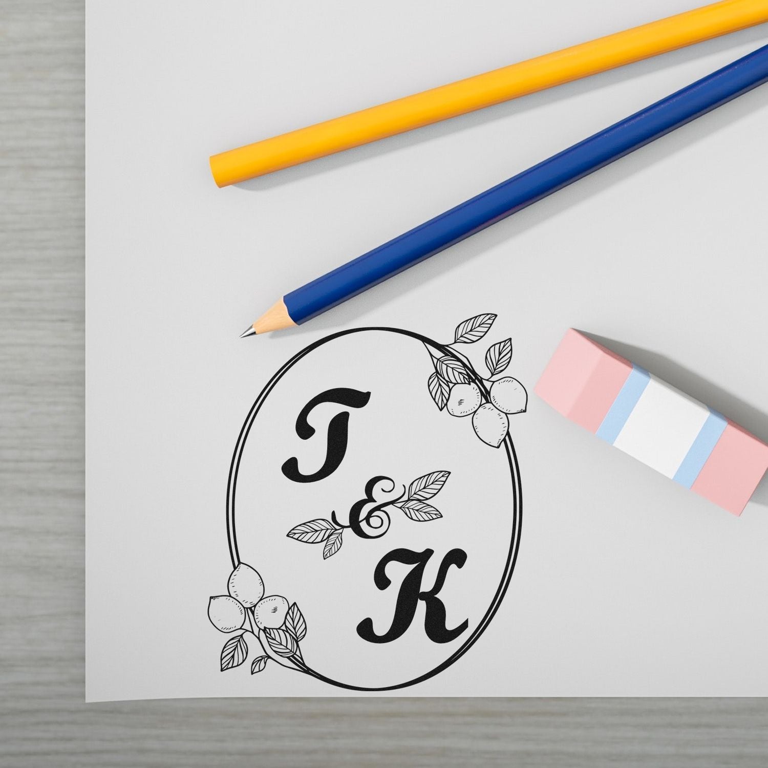 Custom black floral monogram stamp and seal with initials J and K, plus yellow and blue pencils and a pink eraser.