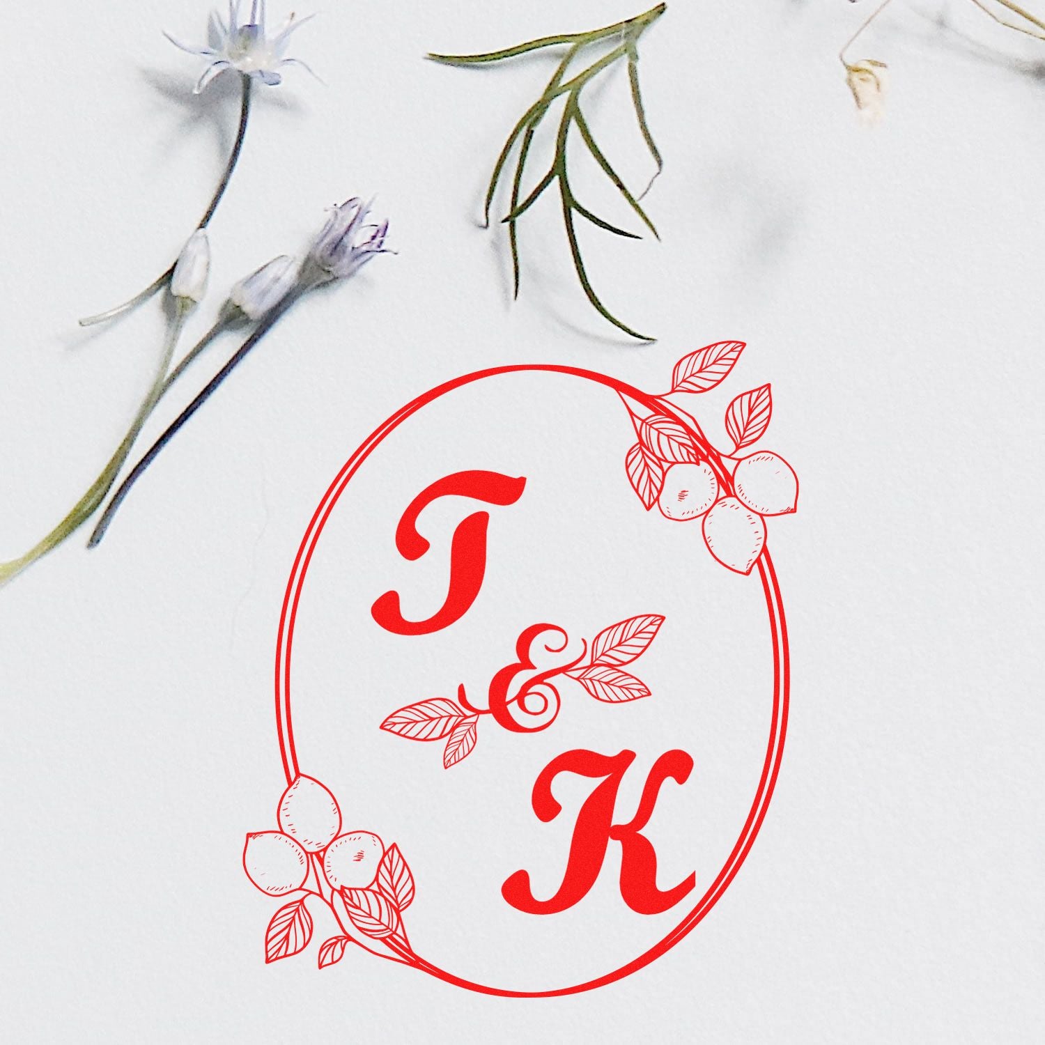Red floral monogram J & K stamp seal with oval border, leaves and berries on a white background.