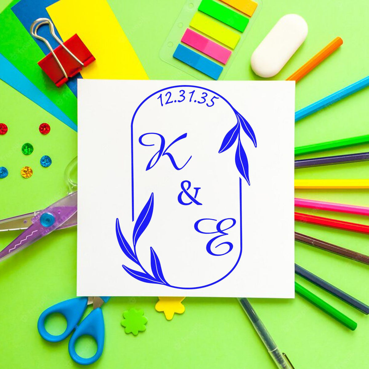 Blue custom stamp and seal design with leafy monogram on white card, surrounded by colorful stationery on a green background.