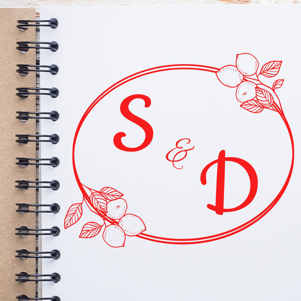 Red custom stamp seal with S and D monogram, floral leaf accents, on white spiral notebook page with black binding.