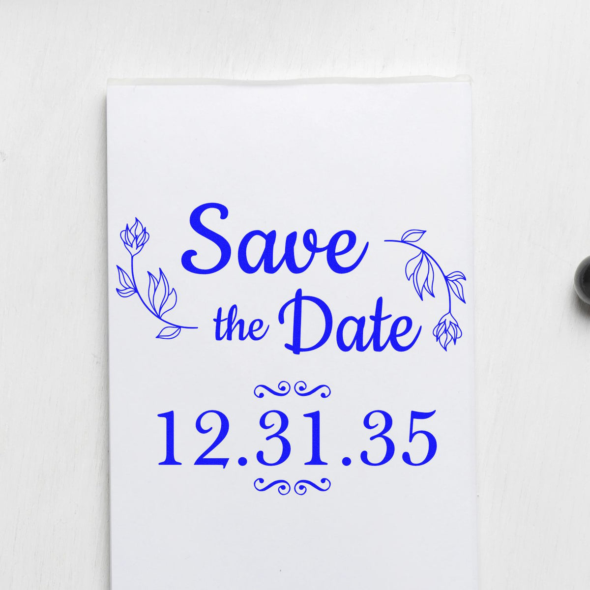 Blue custom rubber stamp/seal design reading Save the Date 12.31.35 with floral accents on white paper.