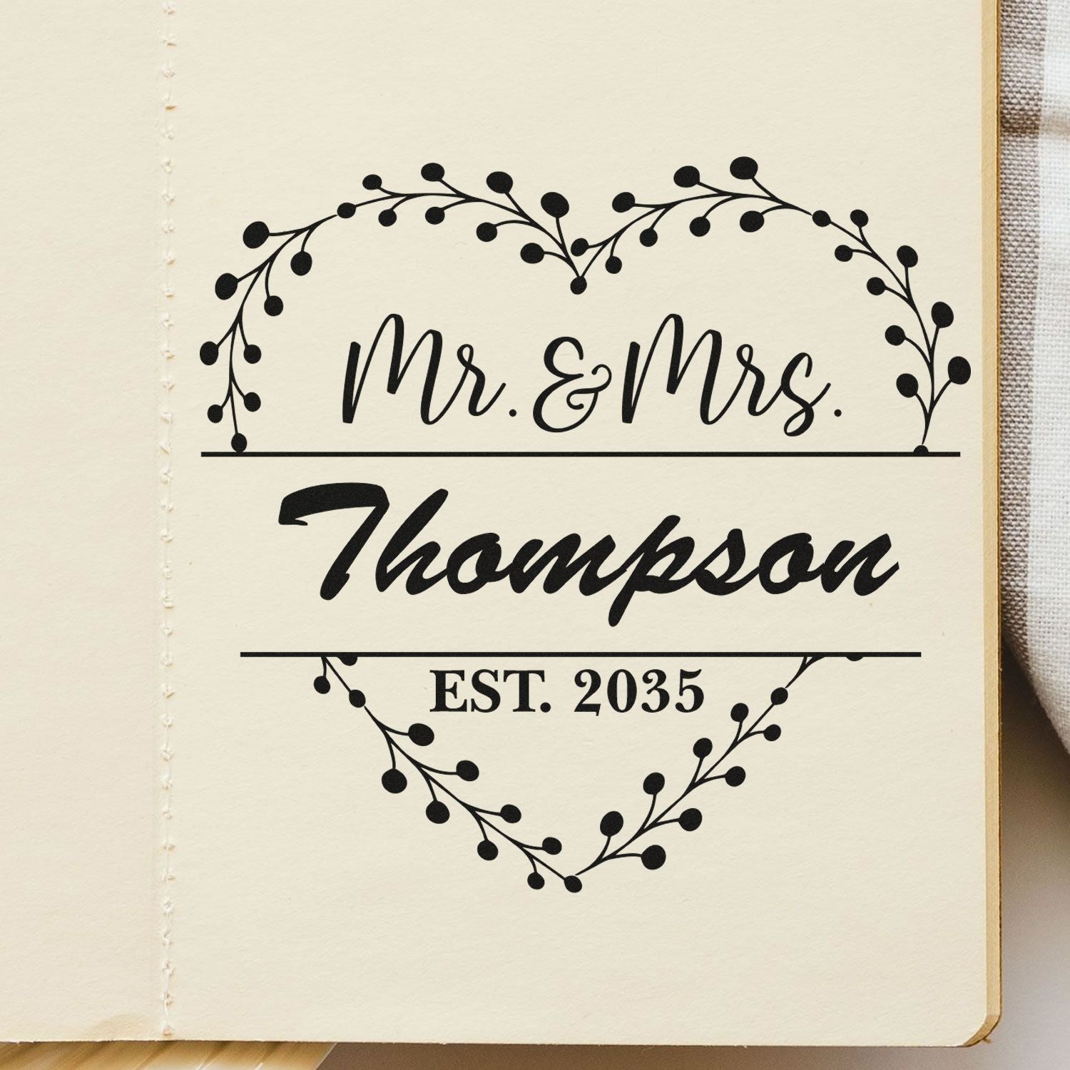 Black custom wedding stamp seal with floral heart wreath, Mr. & Mrs. Thompson and EST. 2035 on cream paper.
