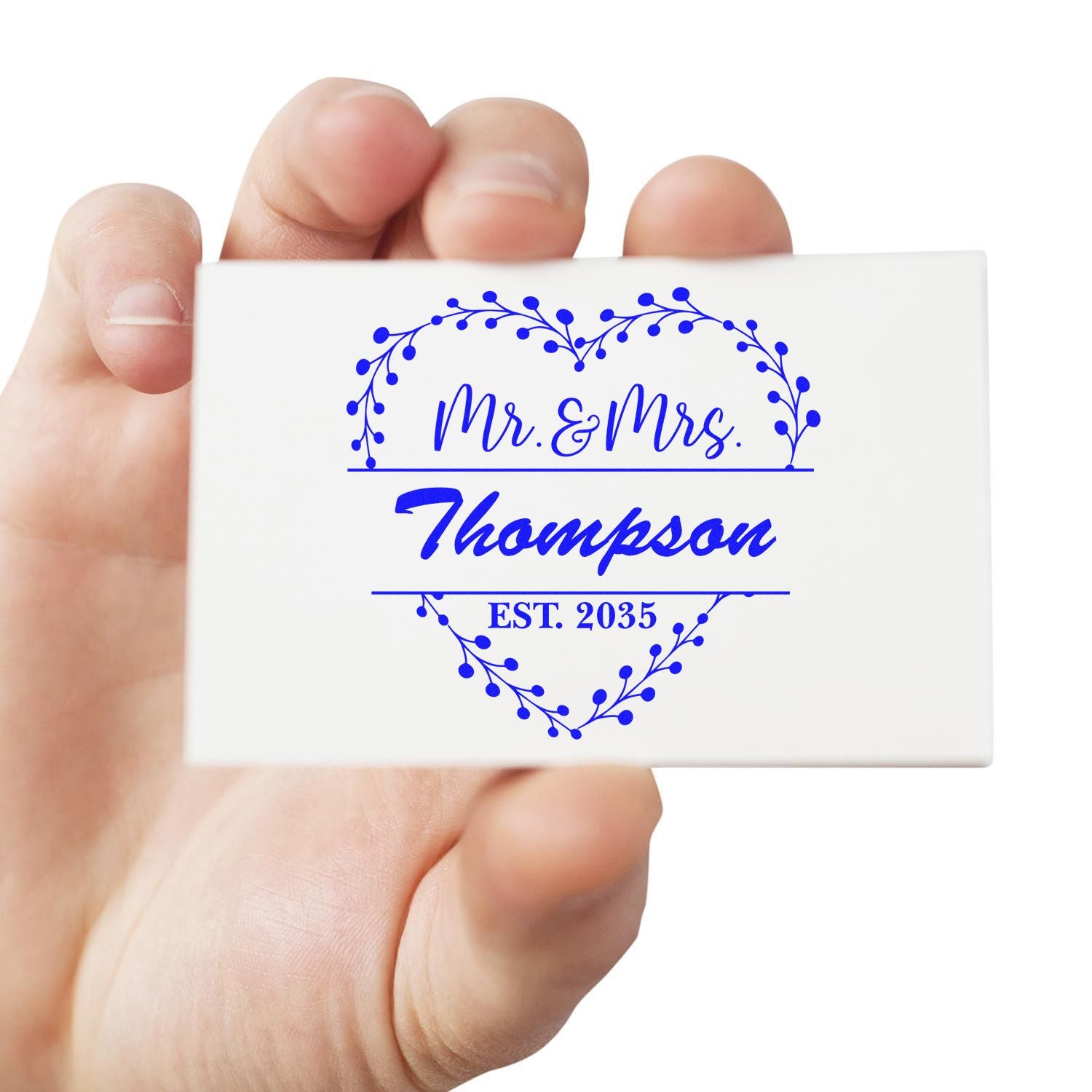 White custom stamp and seal card with blue Mr. & Mrs. Thompson heart wreath design and EST. 2035 held in hand.