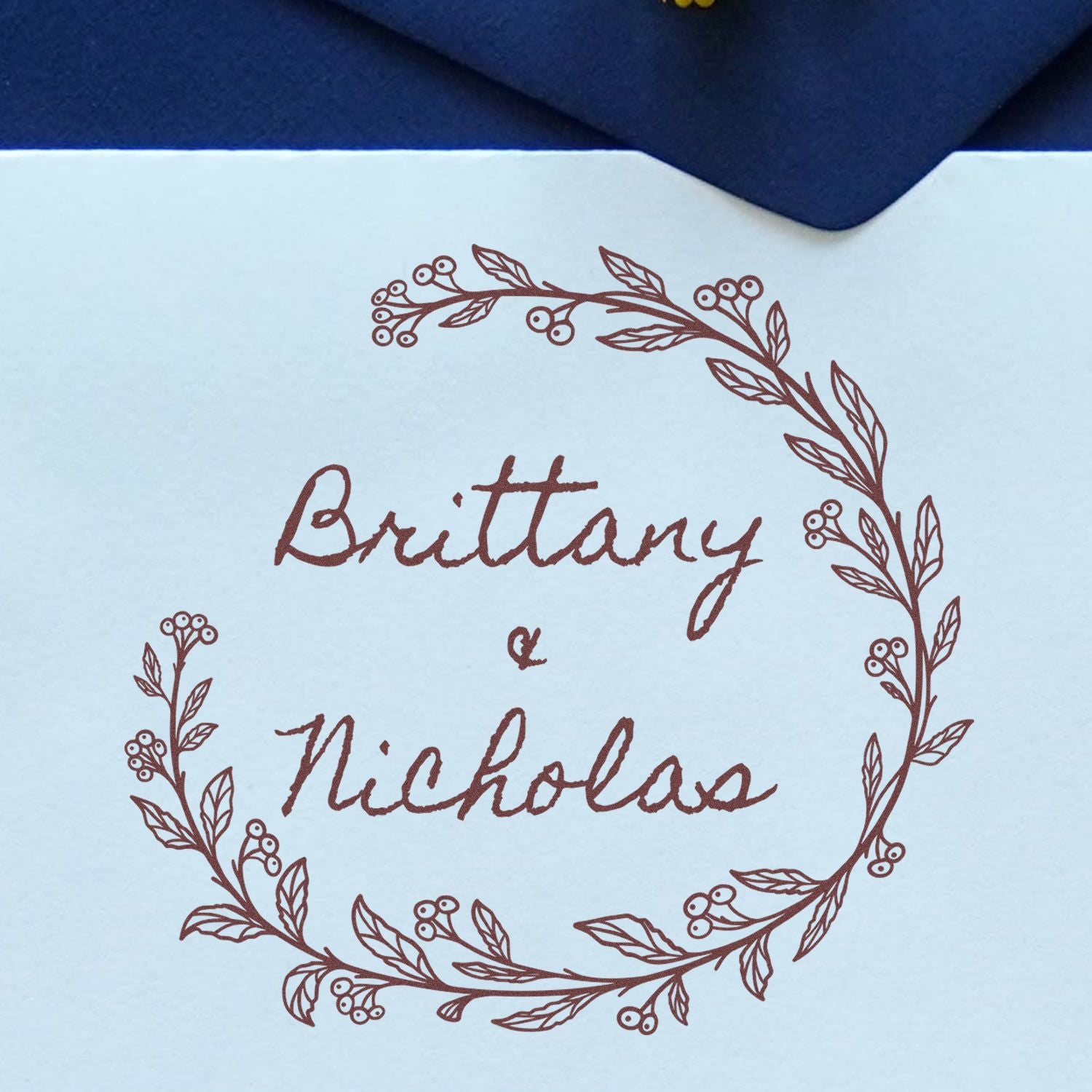 Brown botanical wedding stamp seal reading Brittany & Nicholas on light blue paper with a navy envelope.