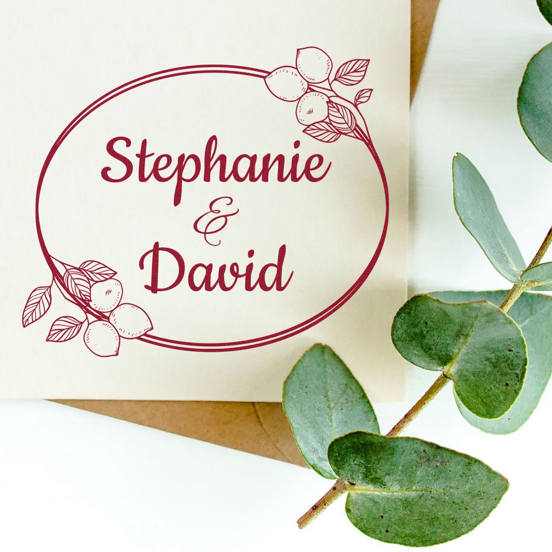 Burgundy custom wedding stamp and seal for Stephanie & David with floral accents on cream paper, beside green eucalyptus leaves.