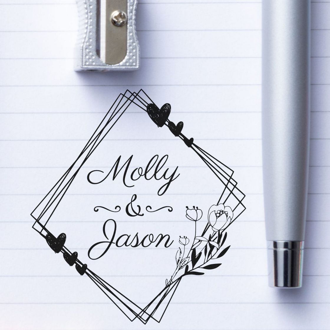 Black custom stamp seal with Molly & Jason in a floral diamond frame, hearts, on lined paper beside a gray pen and silver clip.