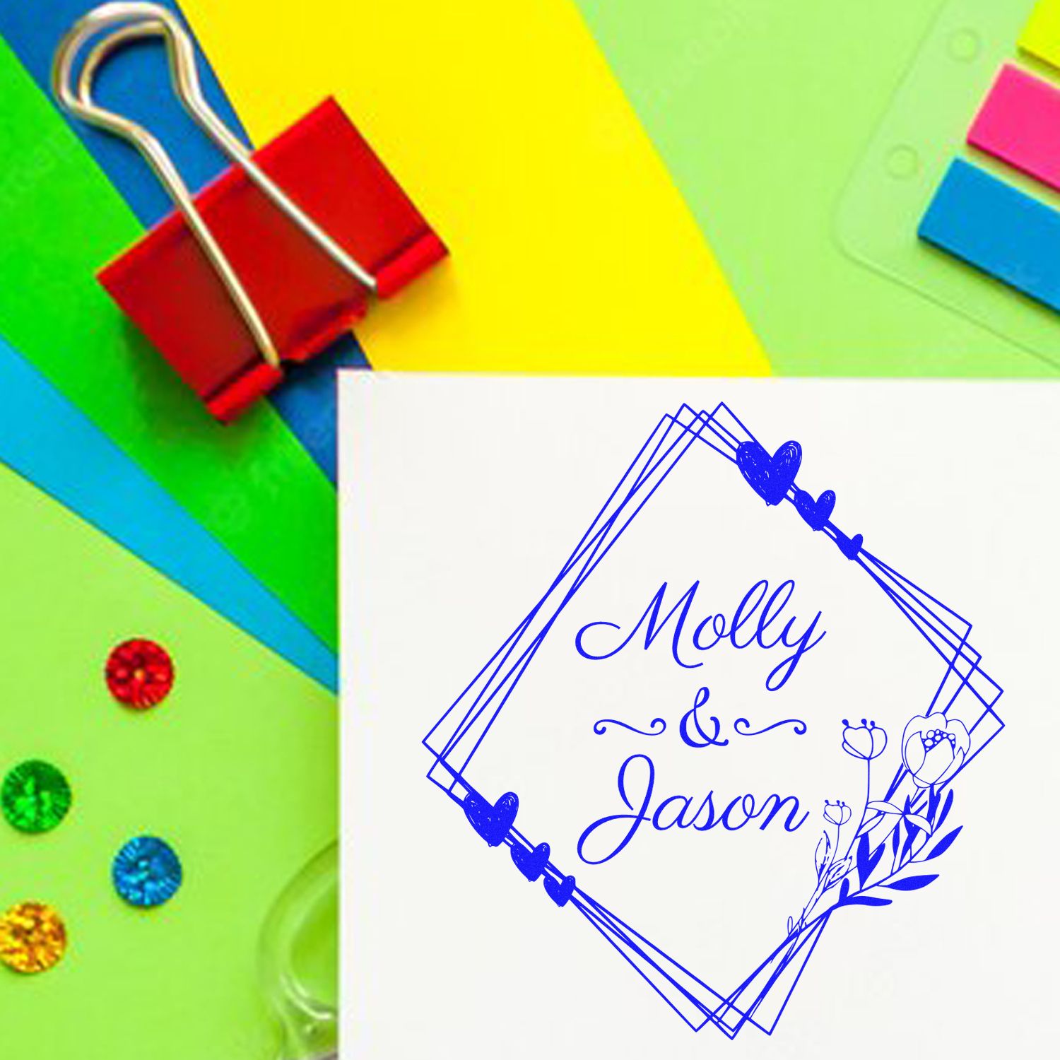 Custom blue wedding stamp and seal with Molly & Jason in geometric frame on white card, surrounded by colorful paper clips and gems.