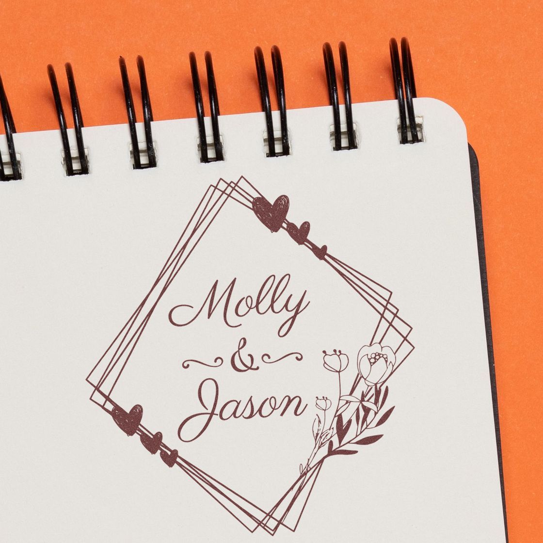 Maroon custom stamp and seal reading Molly & Jason, with hearts and floral accents on a white spiral notebook.