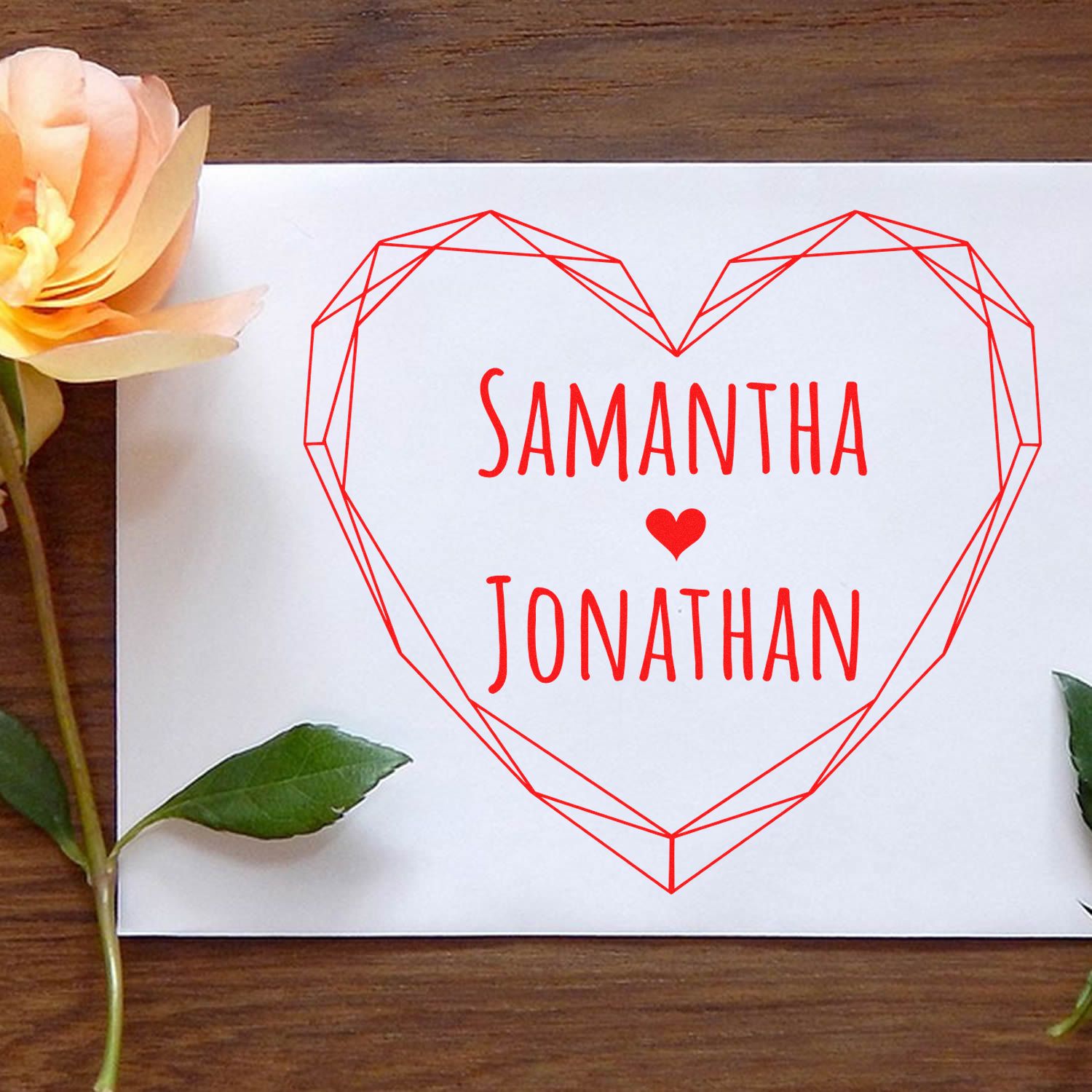 Custom red geometric heart stamp and seal with Samantha ? Jonathan on a white card, styled with flower and green leaves.