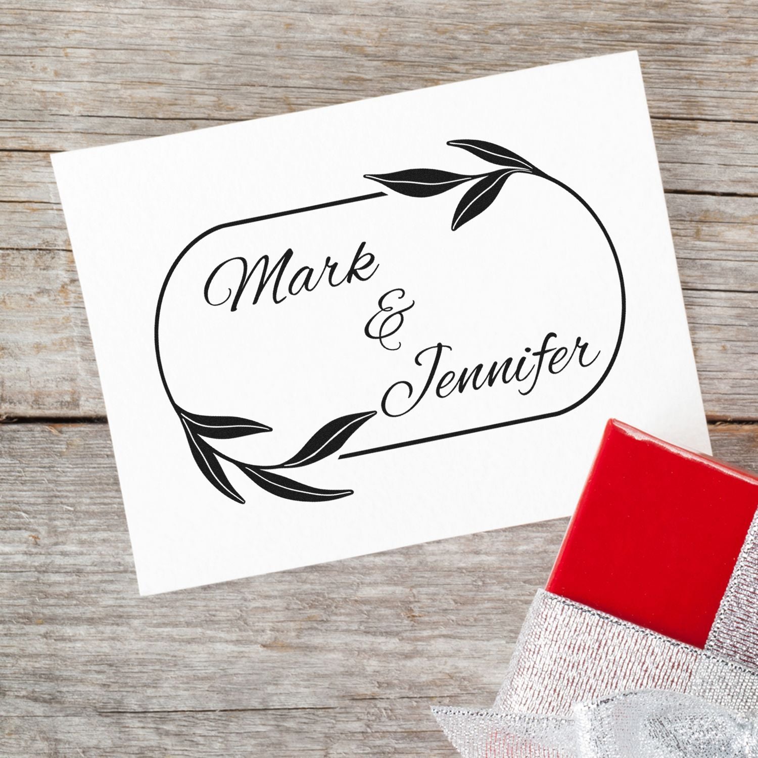 Custom black wedding stamp and seal for Mark & Jennifer with leafy oval design on white card and red stamp block.