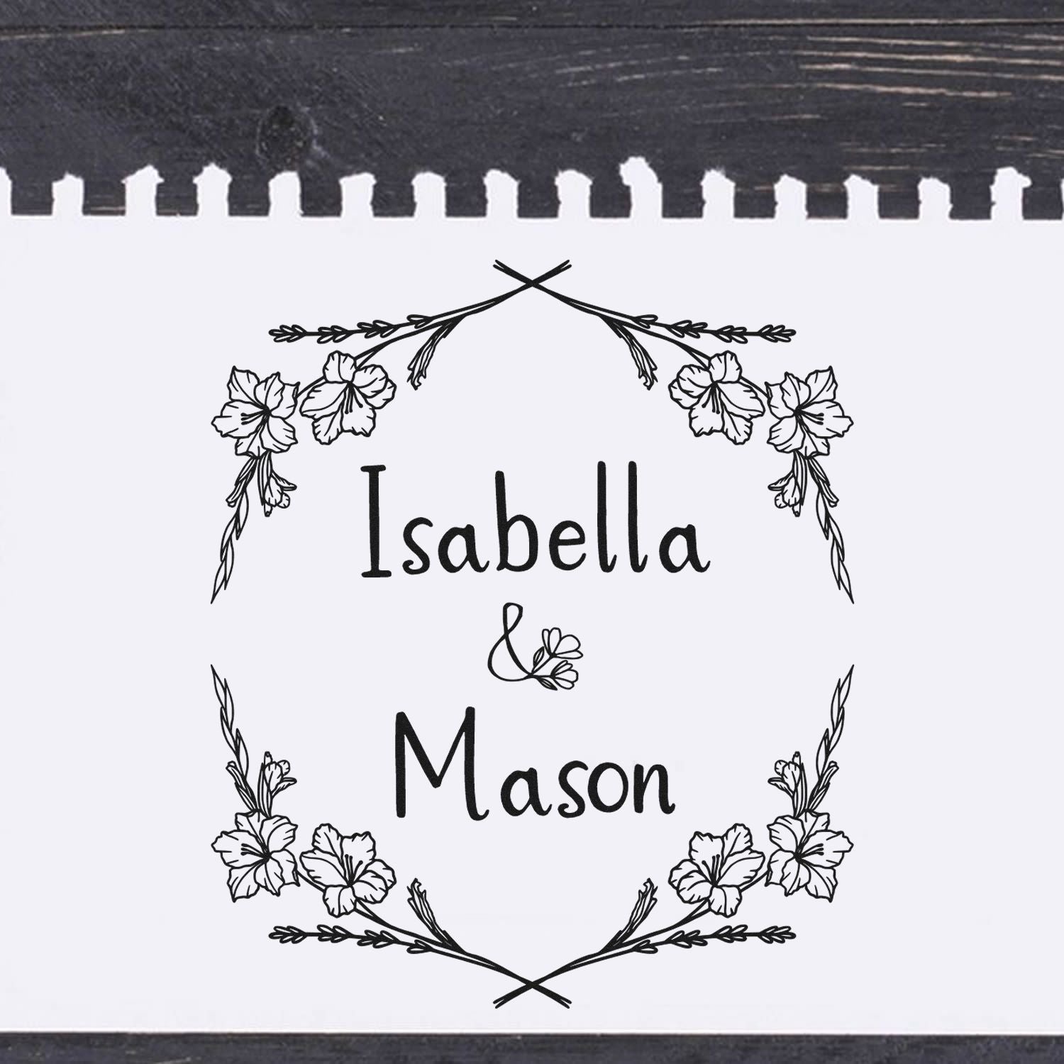 Black-and-white custom stamp seal with floral wreath framing the names Isabella and Mason on white paper.