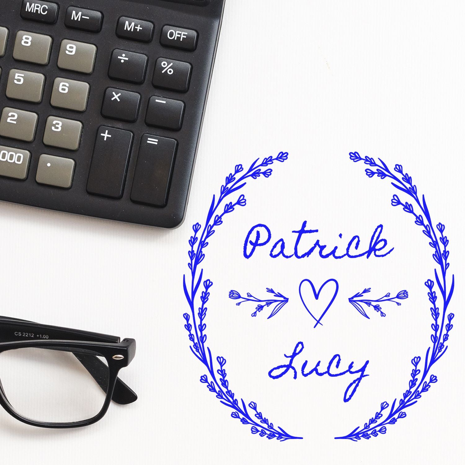 Blue custom stamp seal with Patrick and Lucy, heart and leafy wreath in blue on white, beside a calculator and black glasses.