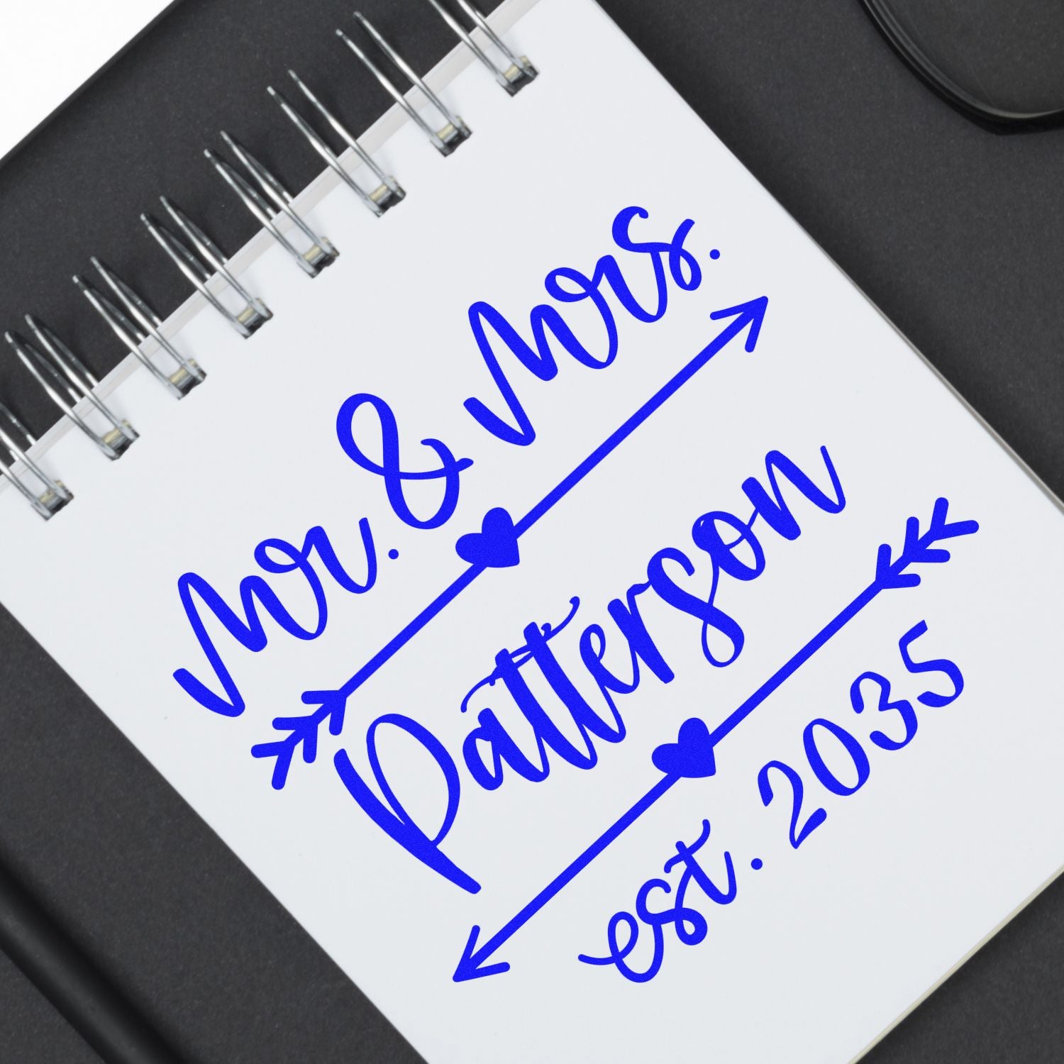Blue custom wedding stamp and seal on white spiral notebook, reading Mr. & Mrs. Patterson with heart arrows and est. 2035.