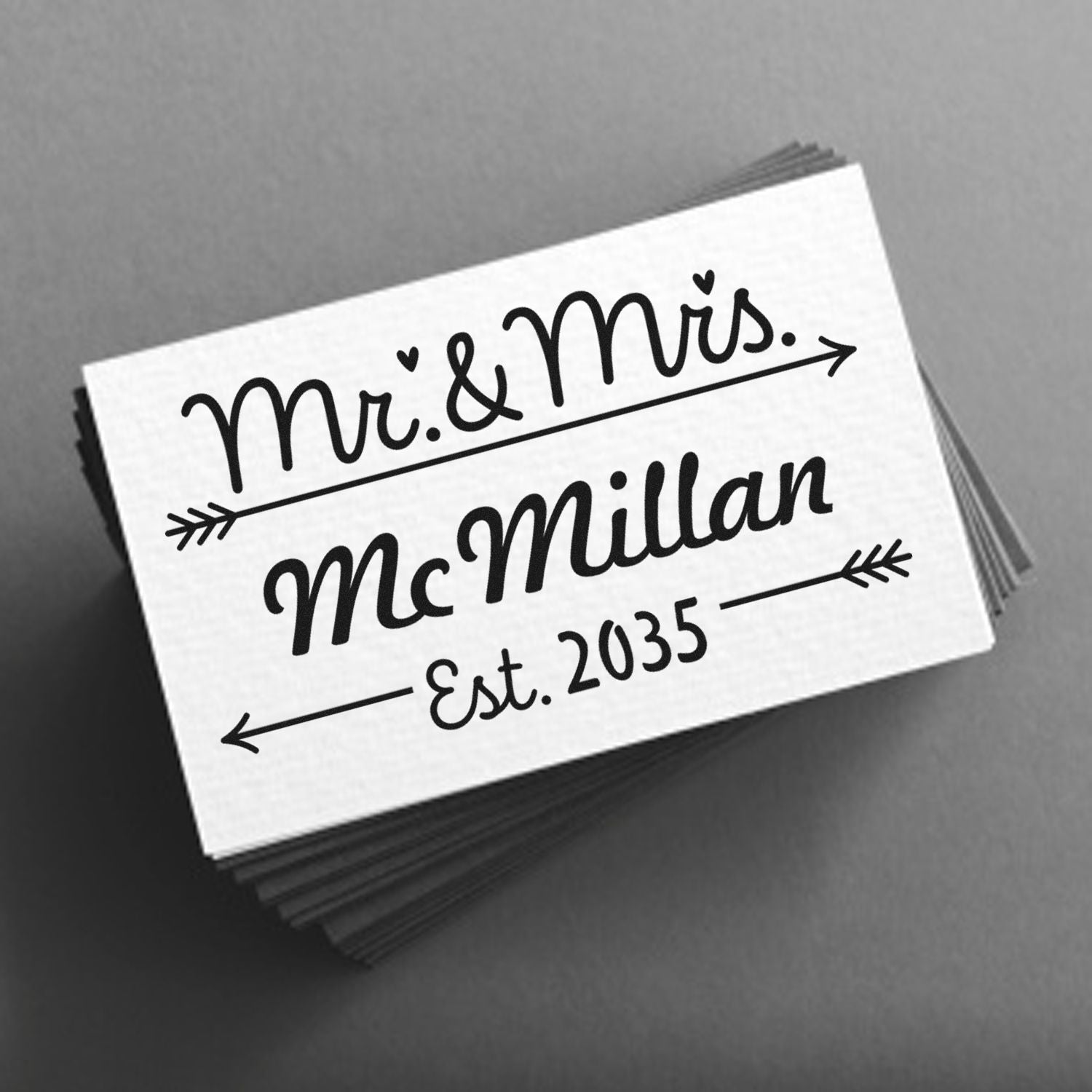 Black custom wedding stamp seal with Mr. & Mrs. McMillan Est. 2035 in black on a white card over a gray background.