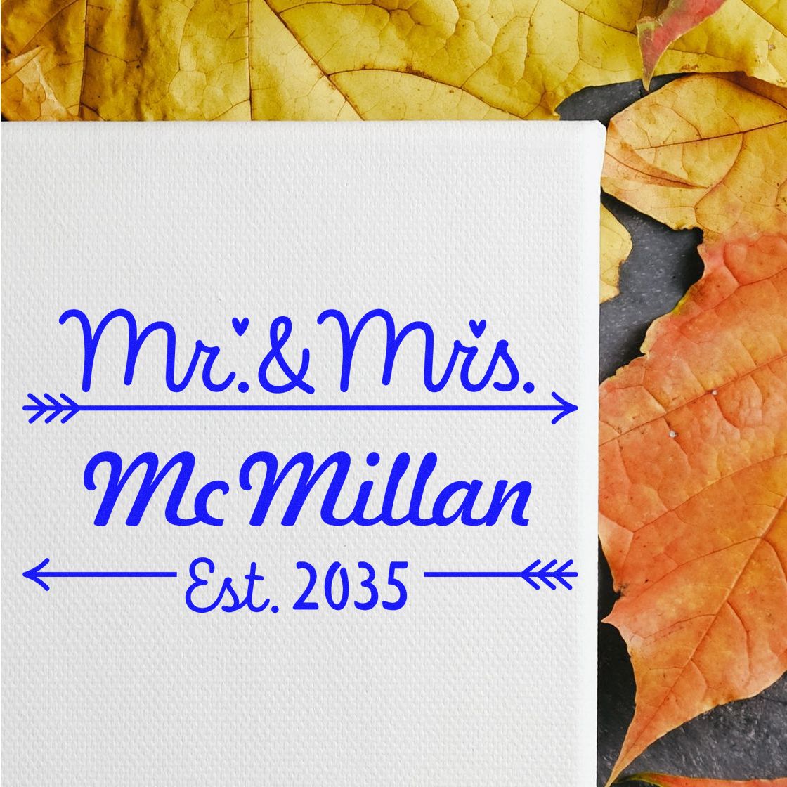Blue custom wedding stamp seal reading Mr. & Mrs. McMillan Est. 2035 on white textured paper with autumn leaves.