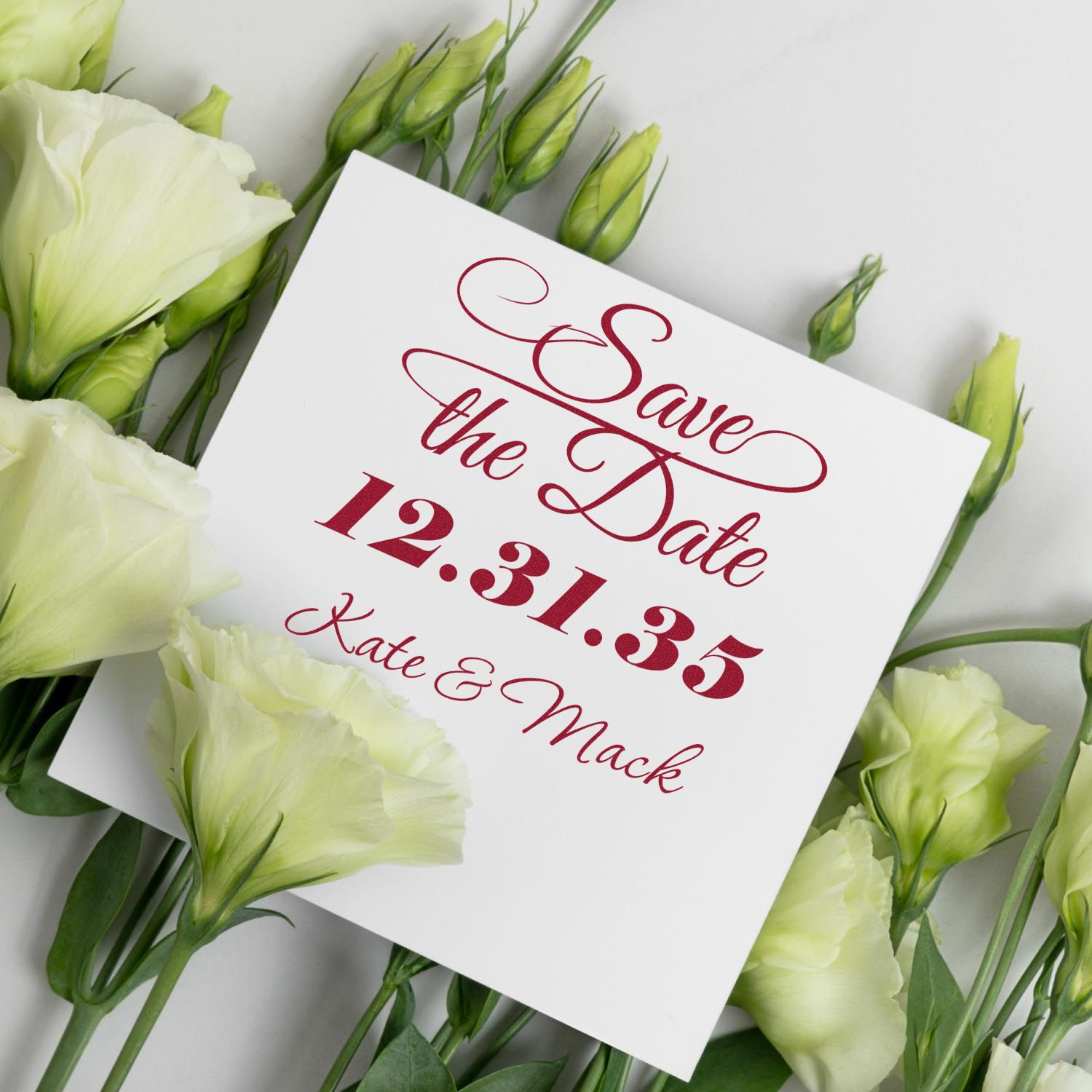 Burgundy Save the Date stamp and seal on white card, surrounded by pale green flowers.