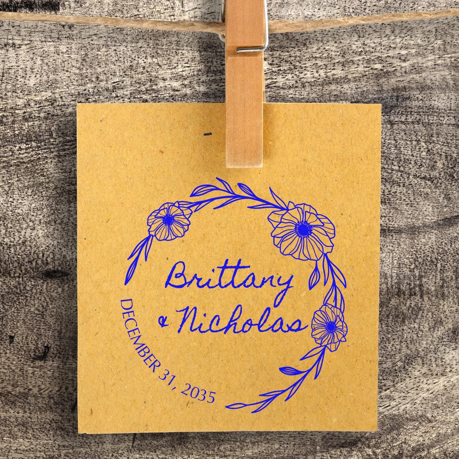 Custom blue floral stamp and seal on kraft paper, with Brittany & Nicholas and December 31, 2035, clipped by wood.