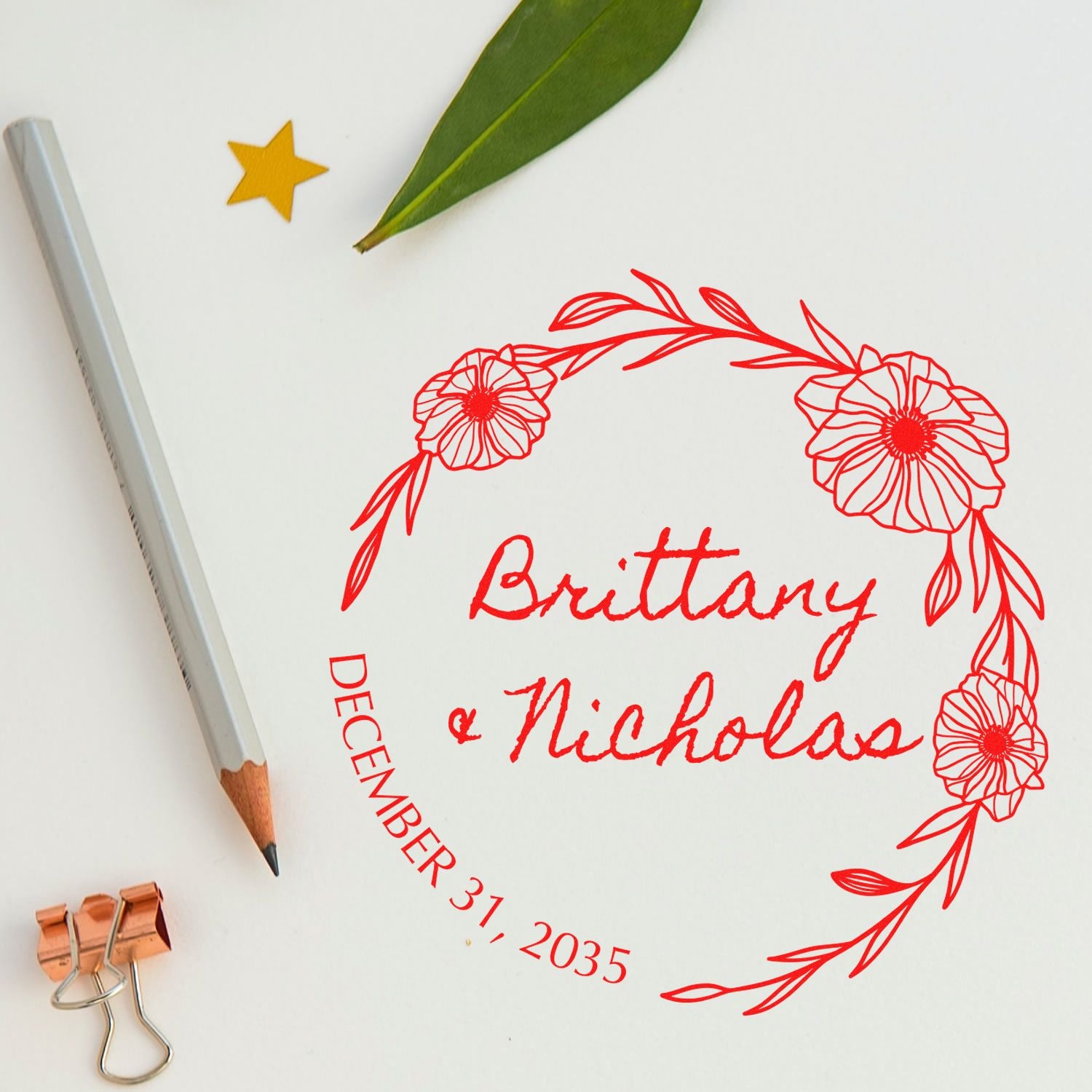 Custom red floral stamp seal reading Brittany & Nicholas, December 31, 2035, beside a pencil, green leaf, and gold star.